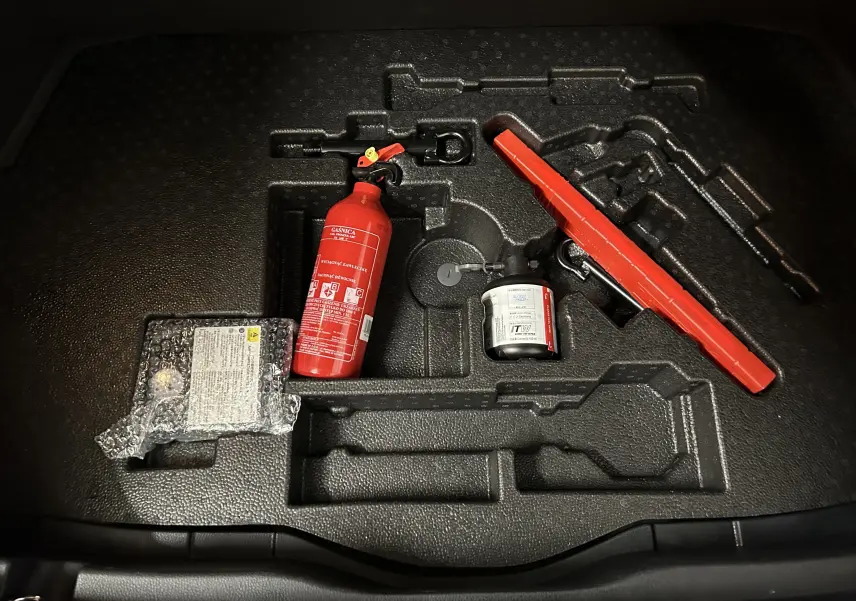 Gros plan sur le coffre du Toyota C-HR Hybride 122h noir métal, montrant extincteur, kit de réparation et triangle de signalisation.