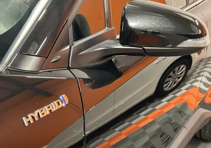 Détail du rétroviseur côté gauche et logo Hybrid sur la porte d’un Toyota C-HR Hybride noir métal.