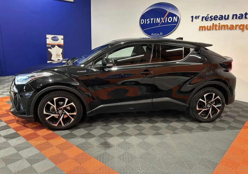 Profil latéral droit du Toyota C-HR Hybride noir métal 2021 avec jantes bi-ton et détails hybrides visibles sur l'aile avant.