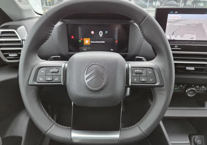 Volant en cuir noir avec commandes intégrées et tableau de bord numérique d'une Citroën C4 hybride 2025 vue de face.