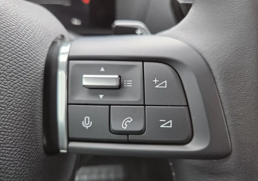 Gros plan sur les commandes au volant du côté gauche du Citroën C4 blanc Okenite, version hybride 2025.