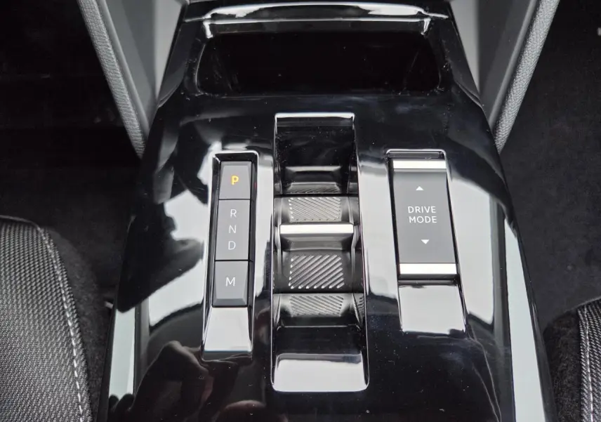 Gros plan sur la console centrale noire brillante de la Citroën C4 hybride 2025 avec commandes de boîte auto et mode de conduite.