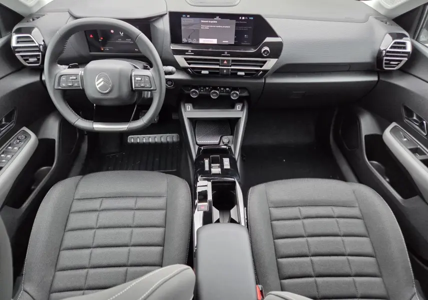 Vue intérieure avant de la Citroën C4 2025, tableau de bord moderne avec écran tactile et sièges tissu noir.