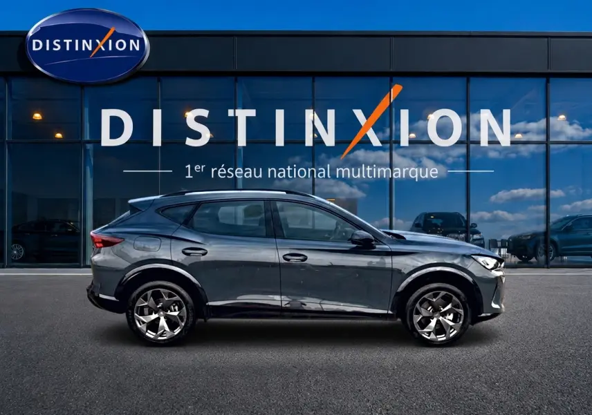 Profil côté gauche d'un CUPRA Formentor 1.5 etsi hybrid 2026 en bleu fjord avec jantes 18 pouces devant une vitrine Distinxion.