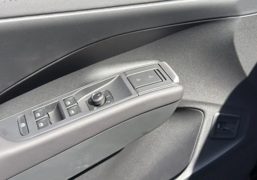 Gros plan sur la commande des vitres et rétroviseurs côté conducteur d’un Volkswagen T-Roc noir 2026.