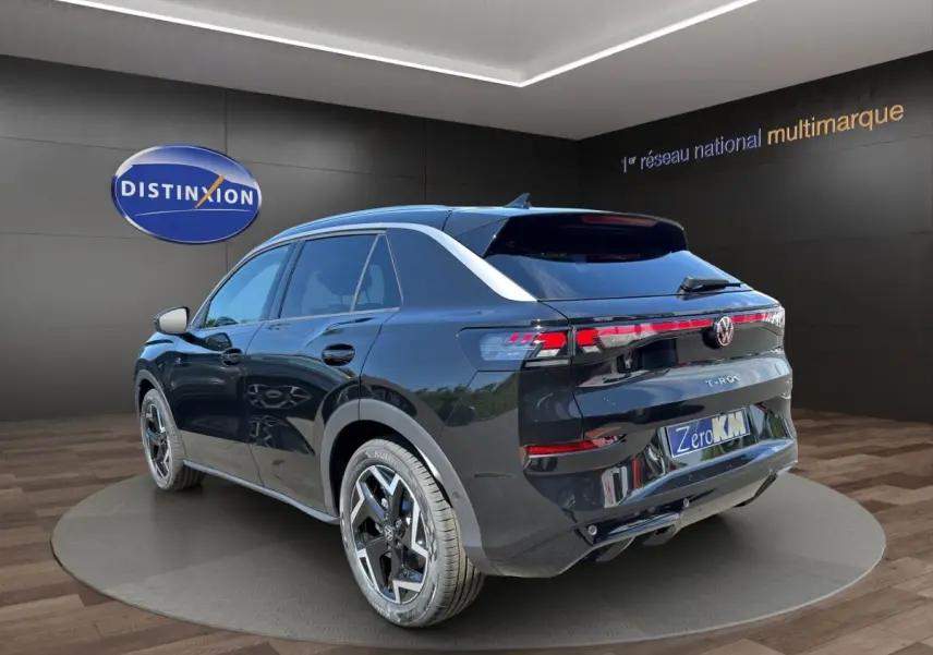 Volkswagen T-Roc noir vu en 3/4 arrière droit, avec feux LED et attelage visible en showroom.