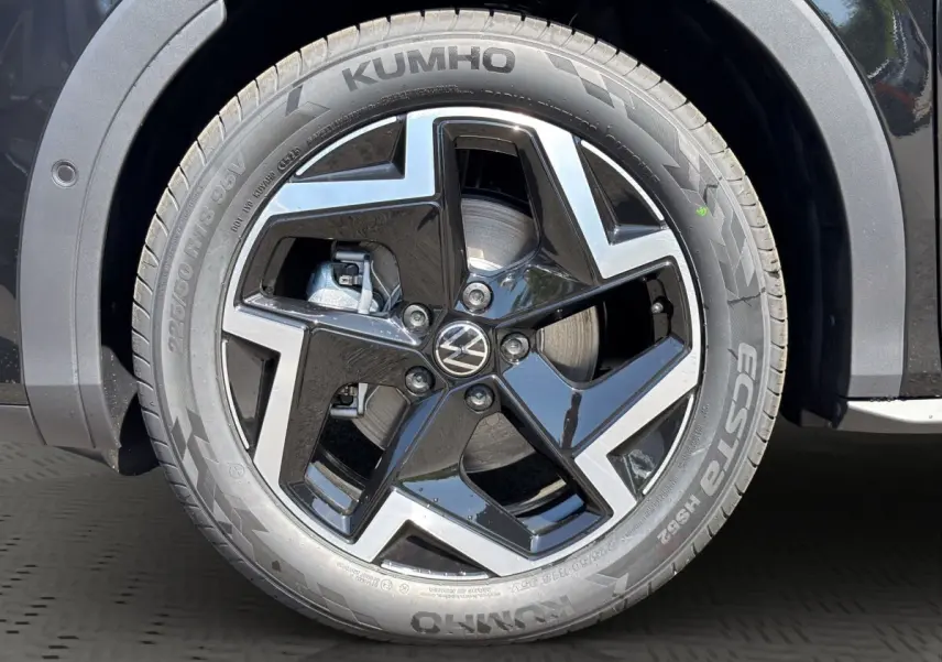 Gros plan sur la roue avant droite noire du Volkswagen T-Roc 1.5 eTSI EVO2 avec jante alliage bicolore et logo VW central.