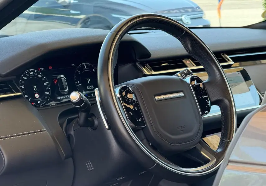 Vue rapprochée du volant en cuir noir du Range Rover Velar 2019 avec tableau de bord numérique et écran tactile.