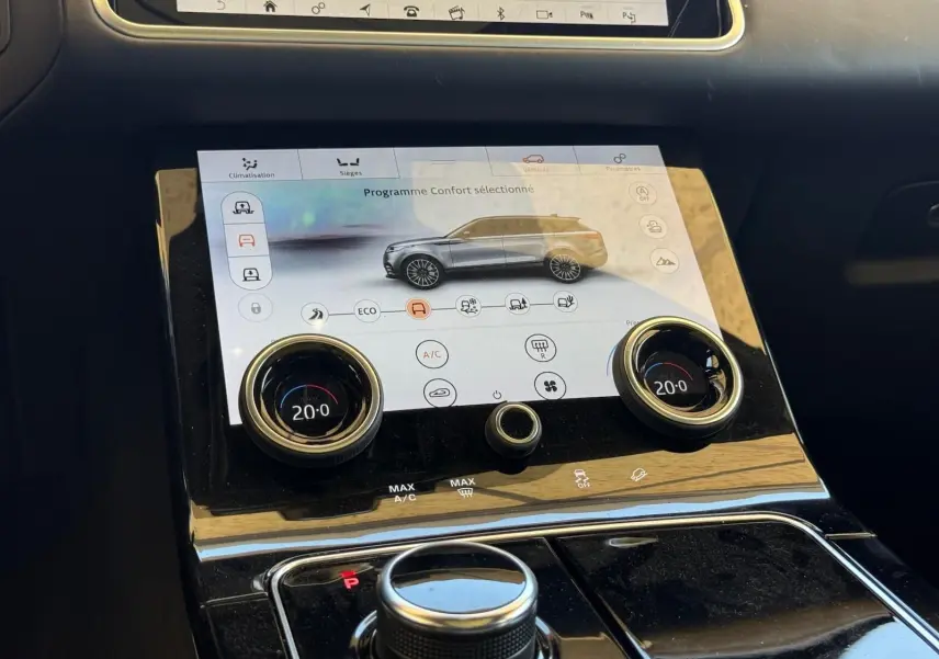 Vue rapprochée de la console centrale du Range Rover Velar gris, avec écran tactile et commandes de climatisation digitales.