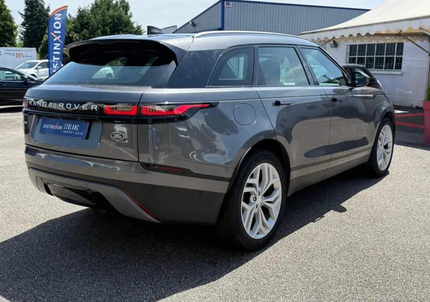 Range Rover Velar gris en 3/4 arrière droit, avec feux LED fins et jantes alliage blanches visibles.