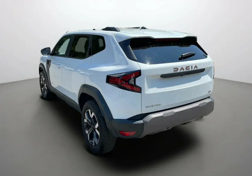 Vue 3/4 arrière droite du Dacia Duster blanc 2025 avec logos distinctifs et protections noires sur les ailes.