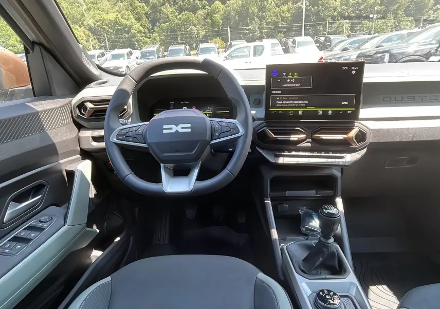 Intérieur du Dacia Duster 2025 blanc, vue frontale du poste de conduite avec volant multifonction et écran tactile.