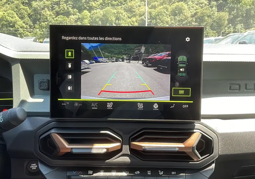 Vue intérieure du tableau de bord du Dacia Duster 2025 avec écran central affichant la caméra de recul et aérateurs hexagonaux bronze.