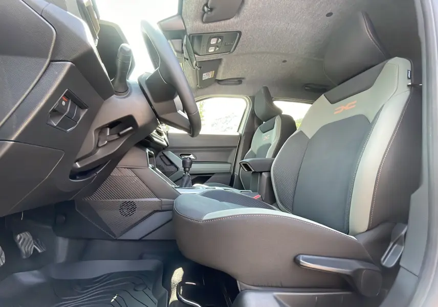 Vue intérieure côté conducteur du Dacia Duster 2025 avec sièges sport bicolores et levier de vitesse manuel.