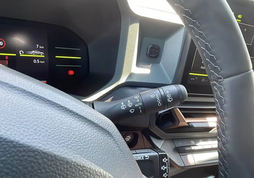 Intérieur du Dacia Duster 2025 blanc, vue rapprochée du tableau de bord et du volant avec commandes intégrées.