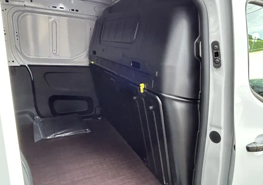 Intérieur du fourgon blanc Peugeot Partner, vue côté droit sur le plancher bois et cloison noire de séparation.