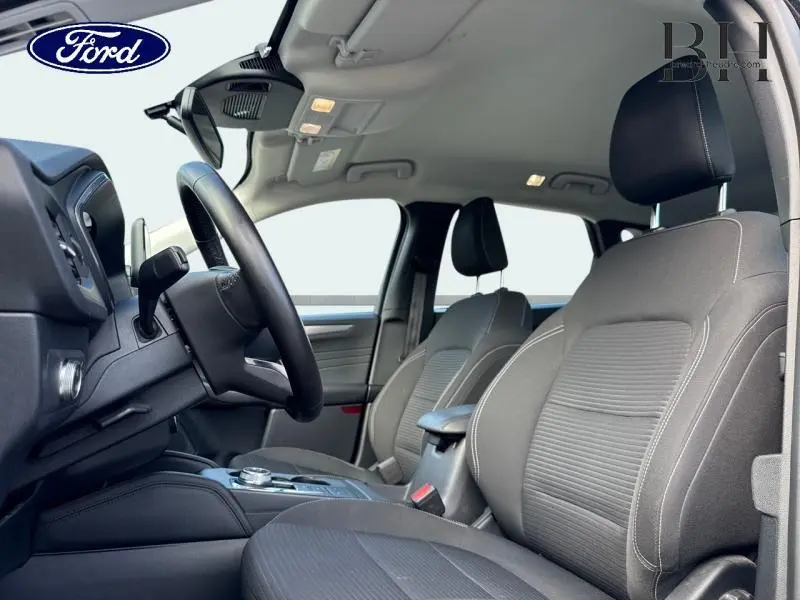 Vue intérieure côté conducteur du Ford Kuga 2023, sièges sport noirs avec volant cuir multifonction.