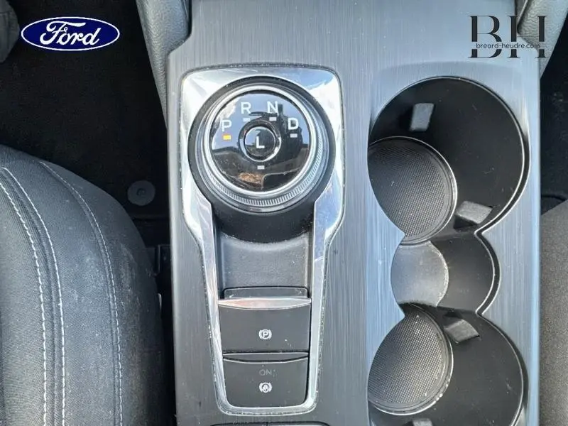 Vue plongeante sur la console centrale noire du Ford Kuga 2023, avec sélecteur rotatif de boîte auto et porte-gobelets.