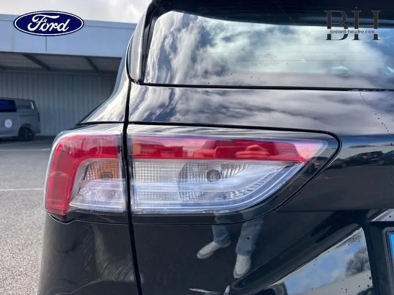 Gros plan sur le feu arrière gauche du Ford Kuga 2023 noir Agate Métallisée avec reflet du ciel sur la carrosserie.
