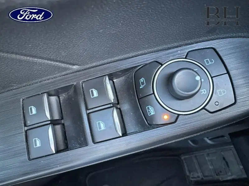 Vue rapprochée du panneau de commandes des vitres et rétroviseurs côté conducteur d’un Ford Kuga noir Agate Métallisée.