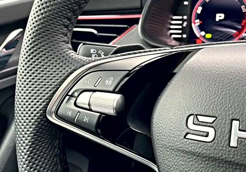 Gros plan sur le volant cuir perforé du Skoda Kamiq blanc nacré, avec commandes multifonctions et palettes au volant visibles.