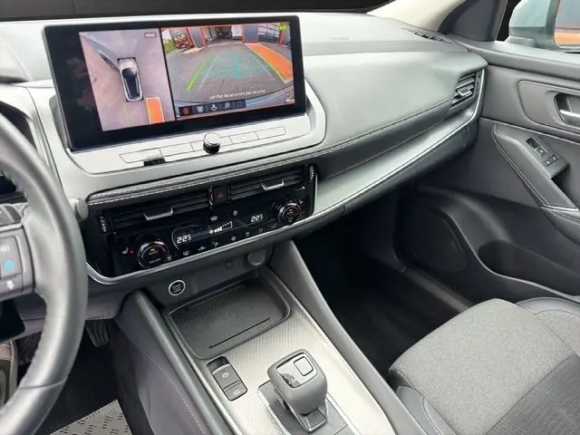 Vue intérieure côté passager du tableau de bord et console centrale du Nissan Qashqai gris foncé avec écran tactile affichant la caméra de recul.
