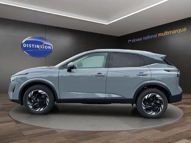 Vue de profil côté gauche du Nissan Qashqai 2025 gris foncé avec jantes noires et toit noir contrasté en showroom.