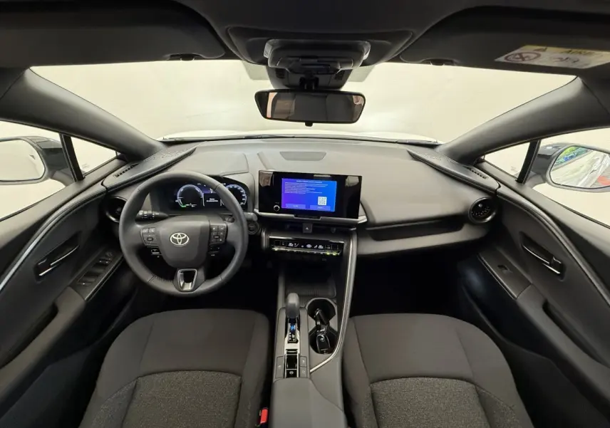 Vue intérieure avant du Toyota C-HR blanc 2024, tableau de bord moderne avec écran tactile et volant multifonctions cuir.