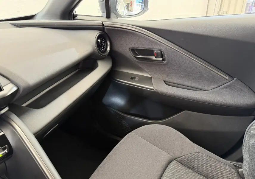 Intérieur côté passager du Toyota C-HR 1.8 Hybride blanc 2024 avec tableau de bord et porte en tissu gris.