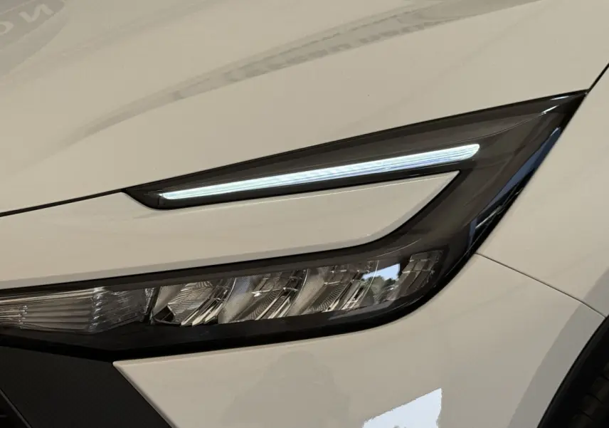 Gros plan sur le phare avant droit LED du Toyota C-HR 1.8 Hybride blanc 2024 avec ligne lumineuse fine.
