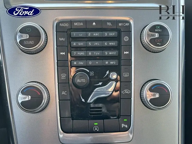 Console centrale de Volvo XC60 D3 2016 en gros plan, boutons de climatisation et multimédia sur fond gris métallisé.