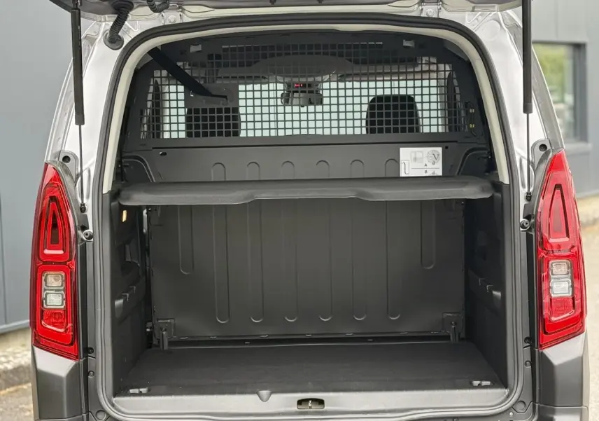 Coffre ouvert vu de l'arrière d'un Citroën Berlingo Multispace gris acier avec lunette arrière ouvrante et séparation grillagée.