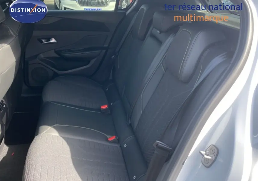 Vue côté droit sur l'intérieur arrière d'une Peugeot 308 blanche, sièges noirs en tissu et cuir avec surpiqûres contrastantes.