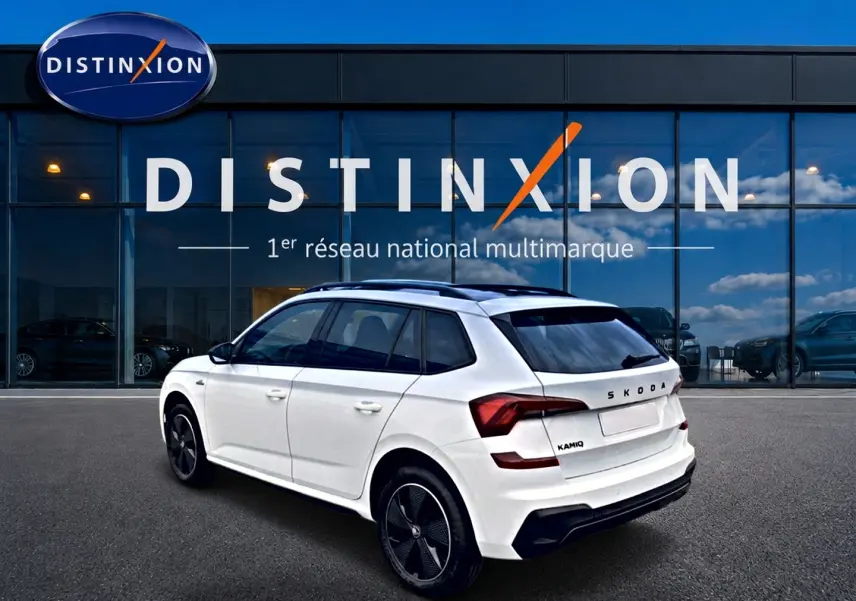 Vue 3/4 arrière droite d'un Skoda Kamiq blanc nacré avec jantes noires et toit panoramique, devant une vitrine Distinxion.