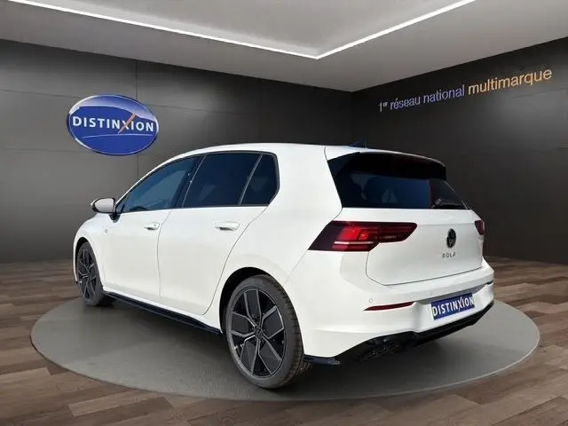 Vue 3/4 arrière droite d'une Volkswagen Golf blanche 2025 finition R-Line avec toit panoramique et jantes noires.
