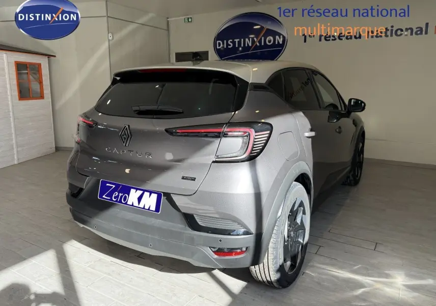 Vue 3/4 arrière droite d'un Renault Captur gris Cassiopée métal avec toit gris, en intérieur showroom.