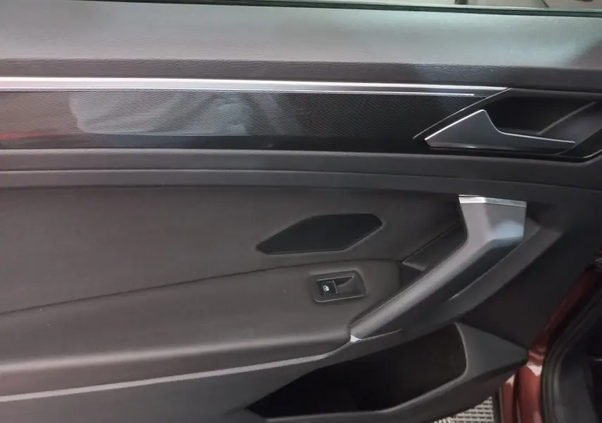 Gros plan sur la porte intérieure côté conducteur du Volkswagen Tiguan Allspace marron, avec poignée argentée et bouton de verrouillage.