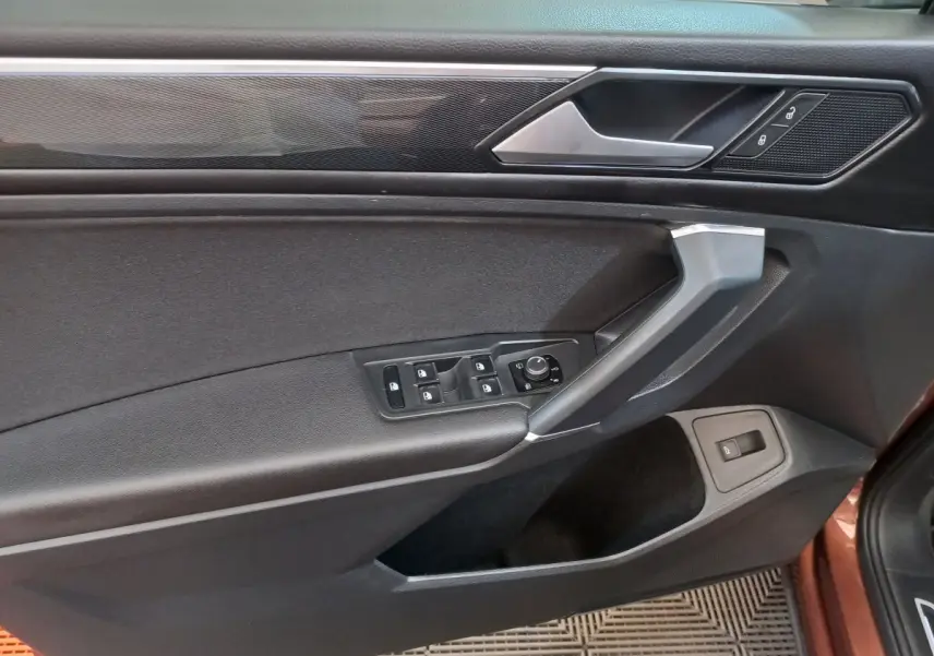 Vue intérieure côté gauche de la porte avant marron du Volkswagen Tiguan Allspace avec commandes vitres et rétroviseurs.