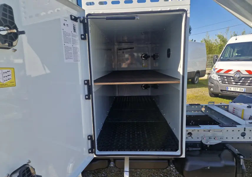 Vue latérale gauche d'un Iveco Daily blanc avec coffre Bawer fixé sur le châssis, benne relevée visible à droite.