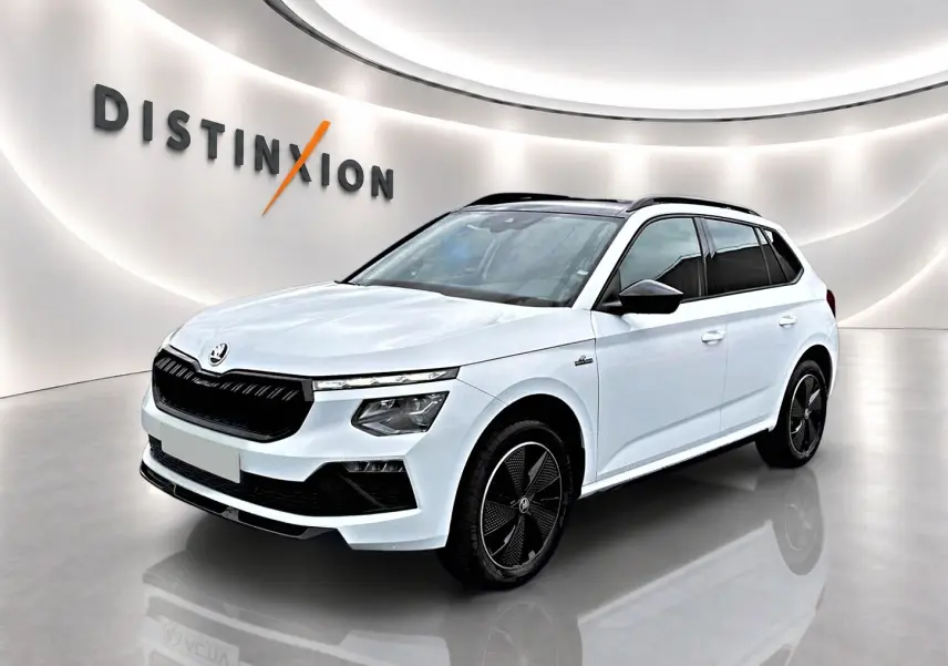 Vue 3/4 avant d'un Skoda Kamiq blanc nacré avec jantes noires et toit panoramique en showroom lumineux.