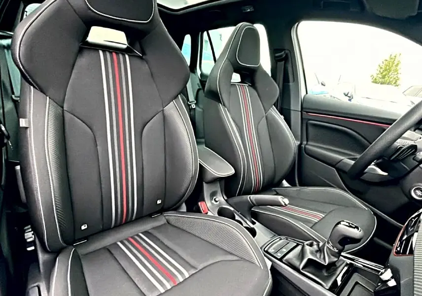 Vue intérieure avant du Skoda Kamiq Monte Carlo 2026, sièges sport noirs avec bandes rouges et grises centrales.