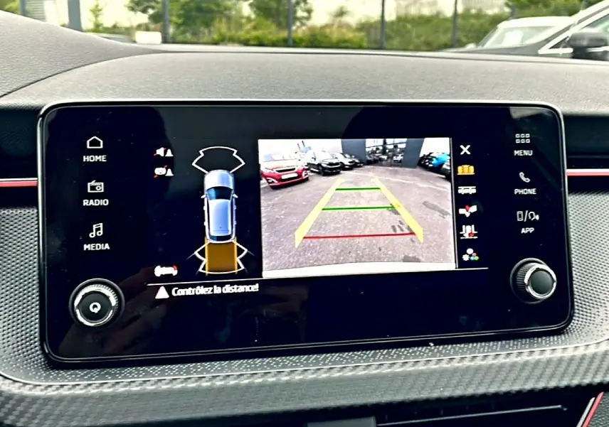 Écran tactile du tableau de bord du Skoda Kamiq blanc nacré montrant la caméra de recul et l’aide au stationnement.