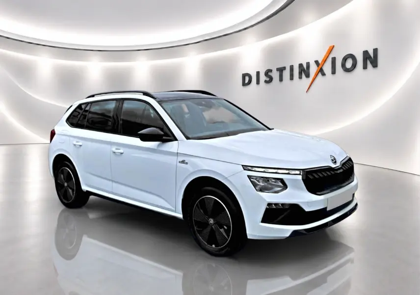 Vue 3/4 avant droite d'un Skoda Kamiq blanc nacré avec jantes noires et toit panoramique en showroom lumineux.