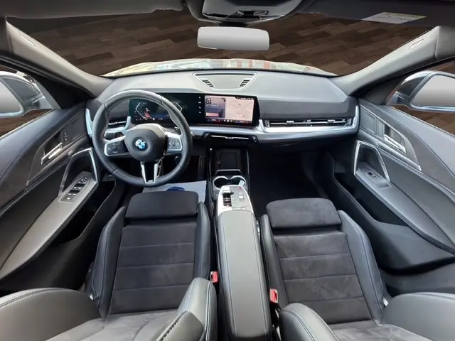 Vue intérieure avant du BMW X2 noir 2025, volant cuir alu multifonctions et écran tactile central large.
