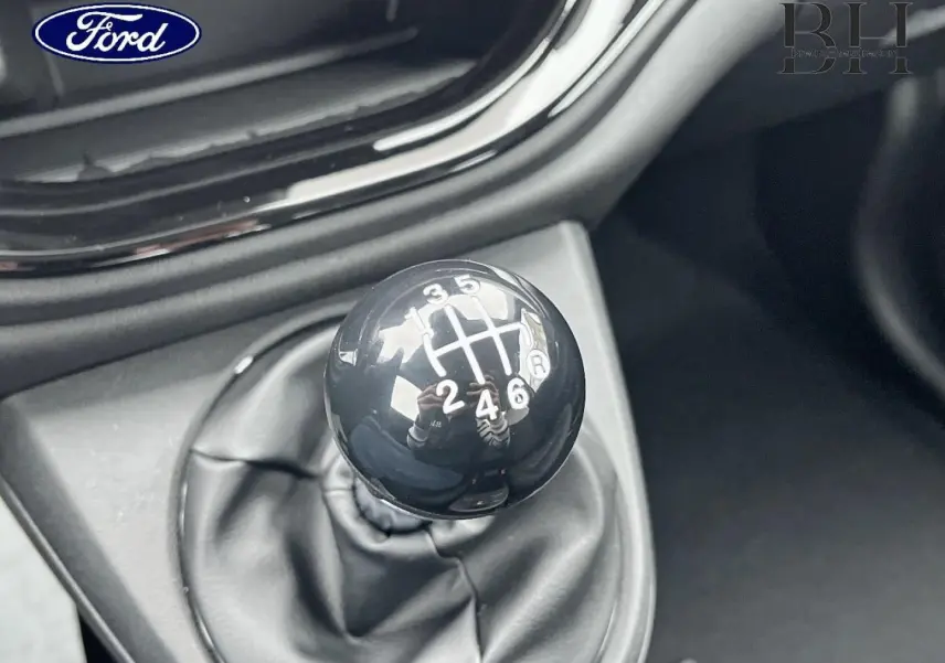 Levier de vitesses manuel noir en gros plan dans l'habitacle d'une voiture, avec console noire brillante visible.