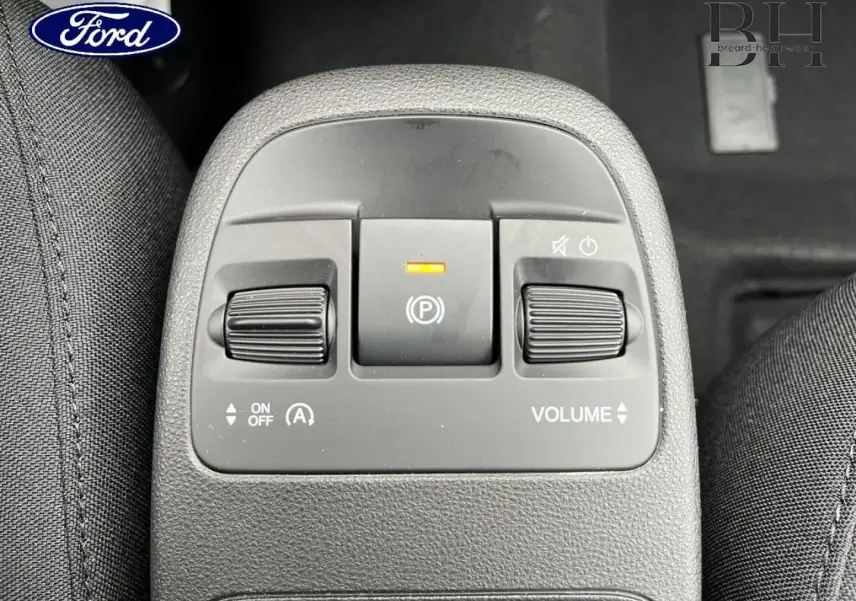 Image montrant le panneau de commandes centrales avec boutons de volume et frein à main électrique, intérieur tissu noir.