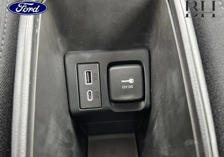 Gros plan sur la prise 12V et ports USB dans le rangement central d’un véhicule, intérieur noir.