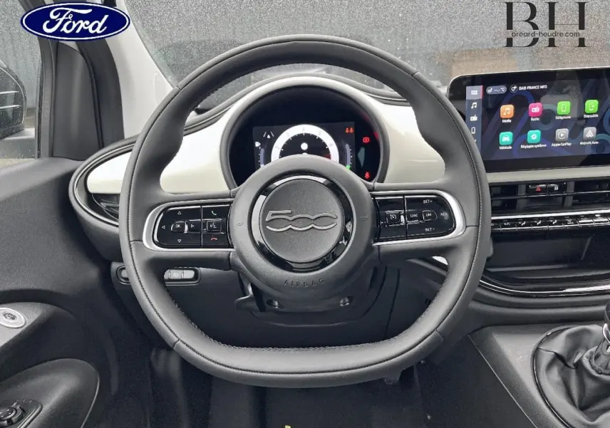 Vue intérieure centrée sur le volant de la Fiat 500 Ice White pastel avec tableau de bord et écran tactile visible.