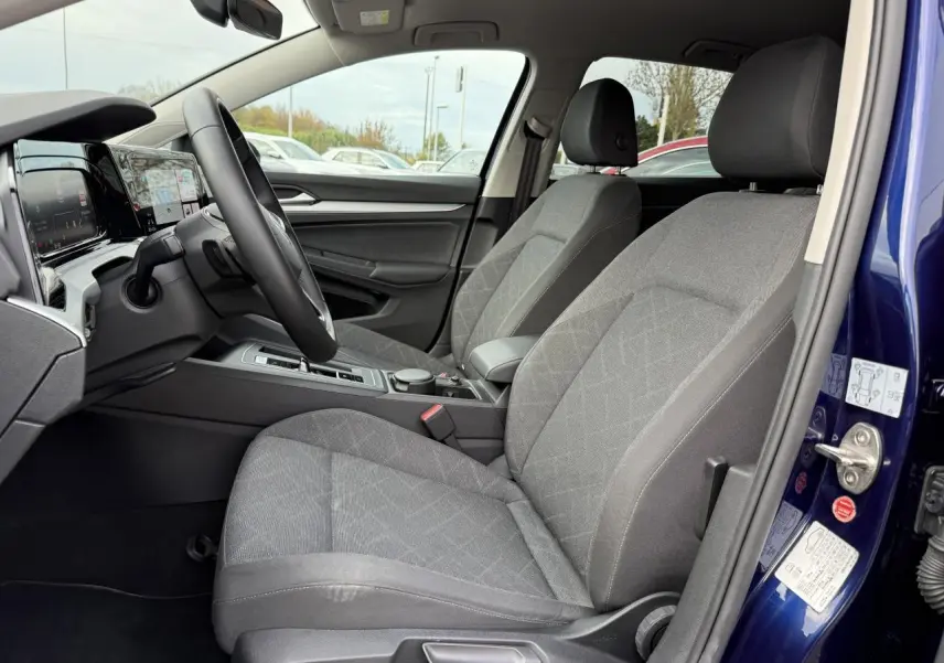 Intérieur côté conducteur d'une Volkswagen Golf 2023 bleu Atlantic, sièges gris et tableau de bord digital.