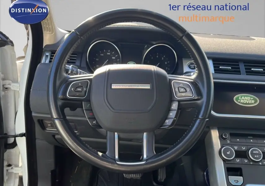 Vue intérieure centrée sur le volant noir du Range Rover Evoque blanc de 2017 avec tableau de bord et écran Land Rover visible.